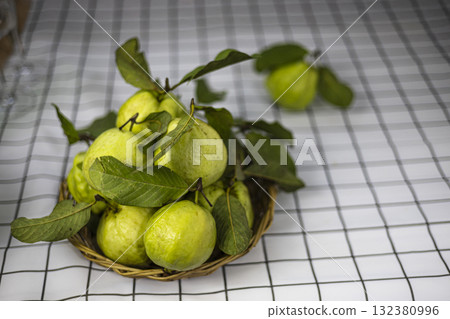 Green Guava In The Bamboo Basket On The Table, Green guavas rest fresh in a rustic bamboo basket on a wooden table, perfect for promoting organic fruit market products. Green Guava In The Bamboo Basket On The Table, Green guavas rest fresh in a rustic bamboo basket on a wooden table, perfect for promoting organic fruit market products. 132380996