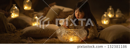 A young girl participates in sound therapy, using a mallet on a crystal bowl while surrounded by softly glowing candles in a peaceful indoor space, banner 132381186