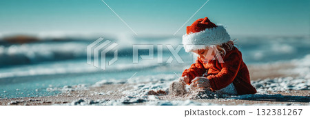 A cheerful toddler digs in the warm sand on a beautiful beach, wearing a bright red Santa hat. The clear blue ocean and sky complete the festive beach scene, banner 132381267