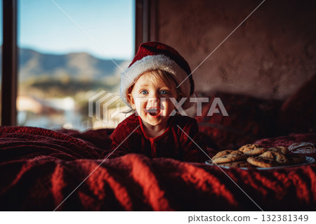 A happy toddler in a festive Santa hat sits on a soft red blanket, laughing with joy. Candy canes are nearby, creating a warm and cheerful holiday atmosphere A happy toddler in a festive Santa hat sits on a soft red blanket, laughing with joy. Candy canes are nearby, creating a warm and cheerful holiday atmosphere 132381349