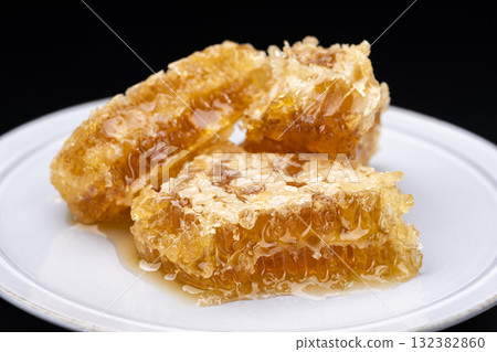 Close-up of a honeycomb overflowing with honey against a black background Close-up of a honeycomb overflowing with honey against a black background 132382860