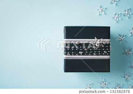 Dark blue gift box decorated with a white ribbon, crystal star, and pearl garland on a light blue background. Copy space. Dark blue gift box decorated with a white ribbon, crystal star, and pearl garland on a light blue background. Copy space. 132382878