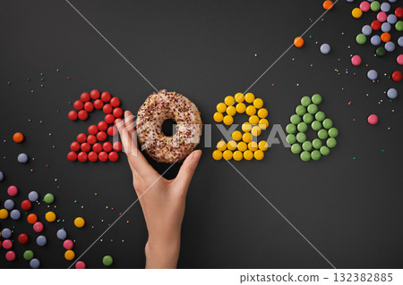 The hand takes a donut from the inscription 2026. New Year's numbers made from sweets. 132382885