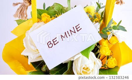 A cheerful bouquet of white roses and yellow blooms sits wrapped in bright yellow paper 132383246