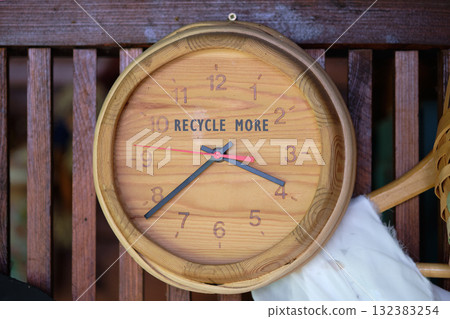 A charming wooden clock adorns a rustic wall, featuring the inspiring message to recycle more. Its simplistic design encourages eco-consciousness in a cozy space A charming wooden clock adorns a rustic wall, featuring the inspiring message to recycle more. Its simplistic design encourages eco-consciousness in a cozy space 132383254