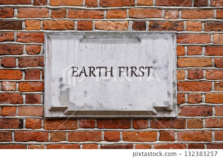 A weathered stone plaque with the words Earth First stands prominently on a textured brick wall, reflecting an emphasis on environmental protection and sustainability in urban landscapes 132383257