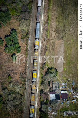 Train crossing over road with houses and greenery in background Train crossing over road with houses and greenery in background 132383374