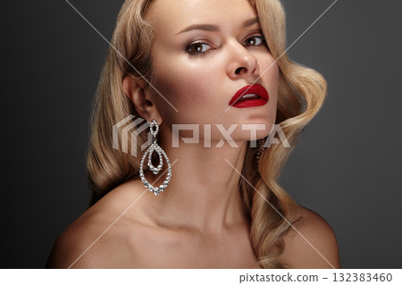 Portrait of a glamorous woman with red lipstick make-up and diamond earrings, flawless makeup, and confident gaze. Elegant studio lighting accentuates luxury and sophistication. Beauty style 132383460