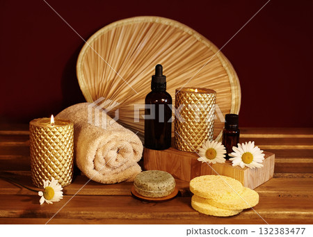 Still life of spa accessories with rolled towels, natural soaps, oils and candles on wooden surface. Warm lighting highlighting textures and neutral tones for wellness and aromatherapy visuals 132383477