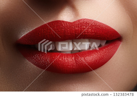 Macro shot of glossy matte red lips parted to show white teeth. Studio-lit close-up emphasizing lip stick texture, shine and color contrast. Ideal for beauty, cosmetology and fashion campaigns 132383478