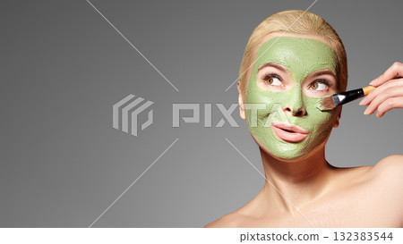 Beautiful Woman Applying Green Facial Mask. Beauty Treatments. Spa Girl Apply Clay Facial mask on grey background Beautiful Woman Applying Green Facial Mask. Beauty Treatments. Spa Girl Apply Clay Facial mask on grey background 132383544