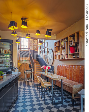 Warm and eclectic interior of a lobby bar with striking checkerboard floor and a cluster of modern pendant lights overhead. Cozy, lived-in atmosphere of modern design with rustic elements 132383887