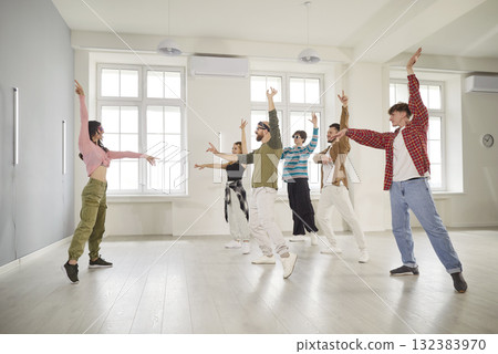 Smiling young people training modern dance moves together in studio with female choreographer. 132383970