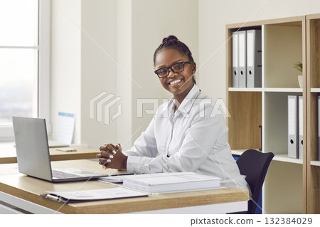 Portrait of happy young African American businesswoman at office desk with laptop Portrait of happy young African American businesswoman at office desk with laptop 132384029