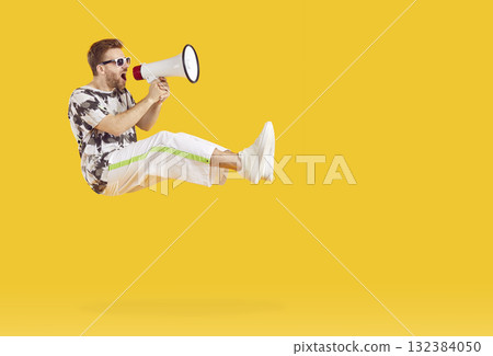 Happy young man jumping and screaming into megaphone 132384050