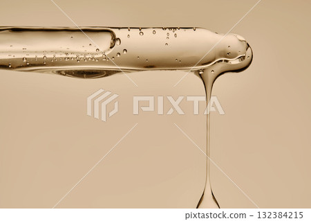 The texture of the serum flowing out of the pipette on a beige background. 132384215