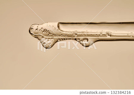 The texture of the serum flowing out of the pipette on a beige background. The texture of the serum flowing out of the pipette on a beige background. 132384216