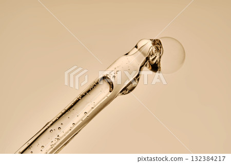 The texture of the serum flowing out of the pipette on a beige background. The texture of the serum flowing out of the pipette on a beige background. 132384217