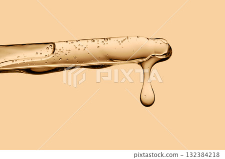 The texture of the serum flowing out of the pipette on a beige background. The texture of the serum flowing out of the pipette on a beige background. 132384218