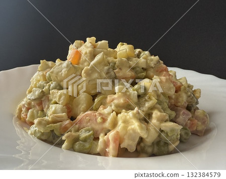 Olivier salad on a white plate. A homemade salad with meat, boiled vegetables, eggs, and mayonnaise. 132384579