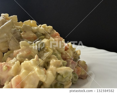 Olivier salad on a white plate. A homemade salad with meat, boiled vegetables, eggs, and mayonnaise. 132384582