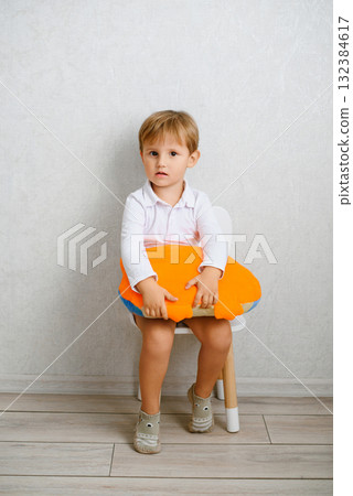 Cute Child Sitting On Chair With Orange Pillow 132384617