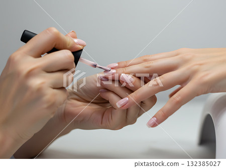 A professional manicurist applying pink nail polish to a client's nails. Close-up of a beauty treatment in a salon. Nail care and cosmetology service 132385027