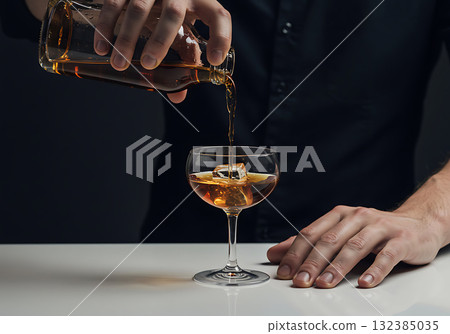Bartender pouring whiskey into a coupe glass with a large ice cube. Close-up of a mixologist preparing a classic cocktail on a dark background 132385035