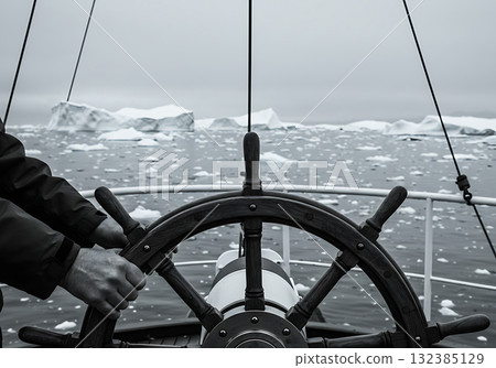 Hands on a ship's wheel steering through an icy sea full of icebergs. Polar exploration and navigation concept. Monochrome photo of an arctic adventure 132385129