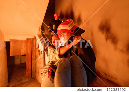 Courageous firefighter carrying a rescued woman down a burning staircase during an emergency evacuation, symbolizing bravery, heroism, and dedication to saving lives in dangerous situations. Courageous firefighter carrying a rescued woman down a burning staircase during an emergency evacuation, symbolizing bravery, heroism, and dedication to saving lives in dangerous situations. 132385392