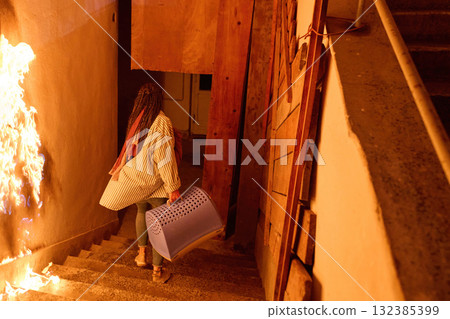 Woman escaping fire with pet carrier, running down stairs in emergency, indoor scene, danger concept, risk and safety, action shot, dramatic lighting, real life situation, hope, fear. 132385399