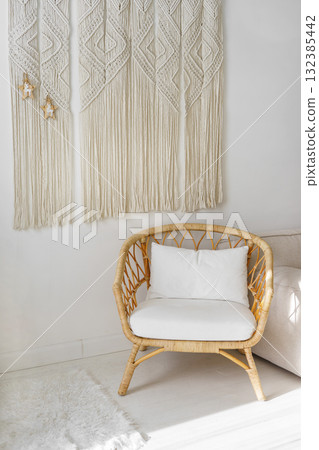 Cozy wicker chair with white pillow and macrame wall hanging in bright minimal boho interior Cozy wicker chair with white pillow and macrame wall hanging in bright minimal boho interior 132385442
