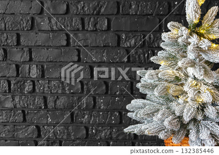 Christmas tree with frost snowy branches decorated with lights on dark brick wall background 132385446