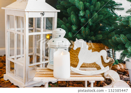 Cozy indoor setting, composition white lantern and wooden decorations on Christmas trees background Cozy indoor setting, composition white lantern and wooden decorations on Christmas trees background 132385447