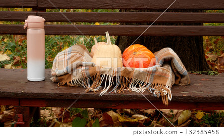 Ripe orange pumpkins in a basket with a cozy brown blanket on a bench 132385458