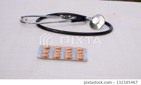 Phonendoscope and blister with tablets on a white surface. 132385467