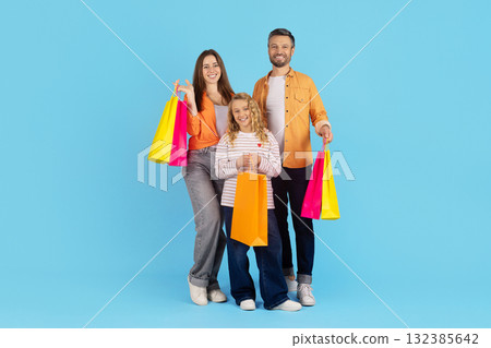 Cheerful family standing together with colorful shopping bags on blue studio background Cheerful family standing together with colorful shopping bags on blue studio background 132385642