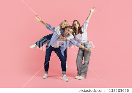 Playful young family having fun on pink background, daughter on fathers back 132385656