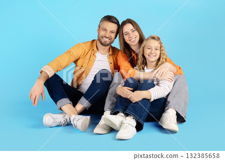 Cheerful family sitting on blue background, hugging and smiling warmly Cheerful family sitting on blue background, hugging and smiling warmly 132385658