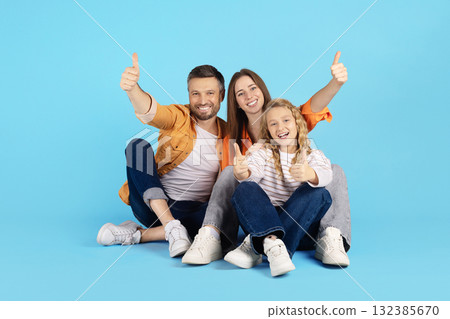 Happy family sitting together on floor in studio, all showing thumbs up and smiling Happy family sitting together on floor in studio, all showing thumbs up and smiling 132385670