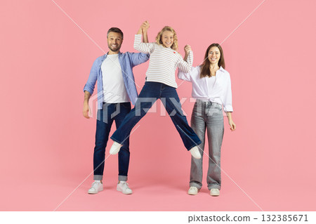 Happy parents lifting daughter in air in studio, playful family moment Happy parents lifting daughter in air in studio, playful family moment 132385671