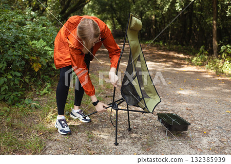 Traveler setting up folding camping chair in forest trail 132385939