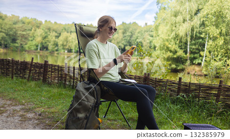 Young woman using smartphone while sitting on camping chair near lake Young woman using smartphone while sitting on camping chair near lake 132385979