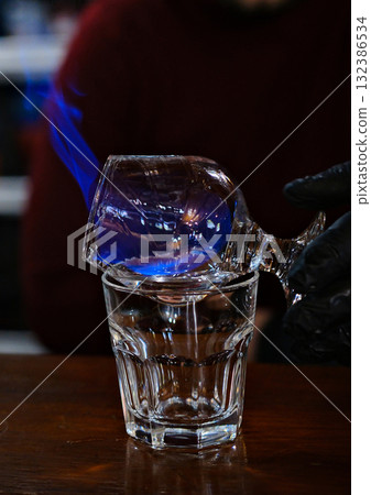 The bartender sets fire to the sambuca in a beautiful wine glass and pours it into another. preparing cocktails at the bar. 132386534
