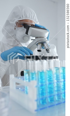 Scientific researcher wearing protective gear adjusting microscope, analyzing lab samples with precision opposite lab tubes in laboratory environment. Medicine, healthcare and science concept Scientific researcher wearing protective gear adjusting microscope, analyzing lab samples with precision opposite lab tubes in laboratory environment. Medicine, healthcare and science concept 132386560