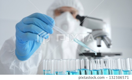 Scientific researcher wearing protective equipment, carefully pipetting liquid into test tubes while conducting medical research experiment. Medicine, healthcare and science concept Scientific researcher wearing protective equipment, carefully pipetting liquid into test tubes while conducting medical research experiment. Medicine, healthcare and science concept 132386571