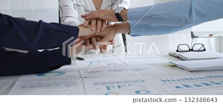 Teamwork and business collaboration with colleagues joining hands over financial charts, symbolizing unity, partnership, success, and strategic corporate planning 132386643