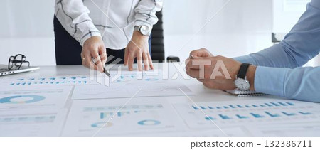 Business team analyzing financial charts and data reports during strategy meeting, hands pointing to documents on table with graphs and diagrams for planning Business team analyzing financial charts and data reports during strategy meeting, hands pointing to documents on table with graphs and diagrams for planning 132386711