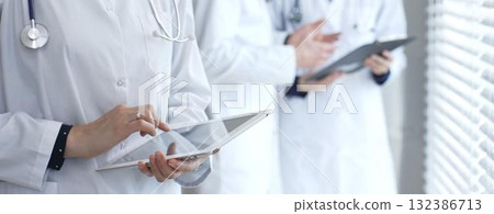 Medical professional using a digital tablet for patient care and data management, collaborating with doctors and healthcare workers in a modern clinic or hospital setting Medical professional using a digital tablet for patient care and data management, collaborating with doctors and healthcare workers in a modern clinic or hospital setting 132386713