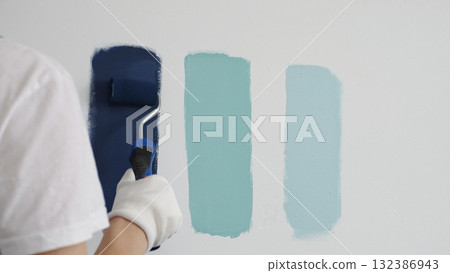 Painter wearing protective gloves rolling blue paint on white wall, creating gradient color effect for home interior renovation project 132386943